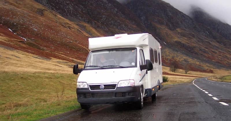 Camper rijdend op een natte weg door mistige heuvels