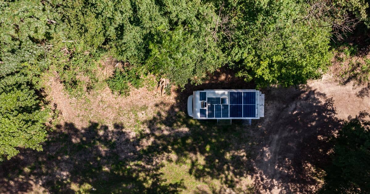 Luchtopname van een kampeerauto met zonnepanelen op het dak, geparkeerd op een open plek in het bos