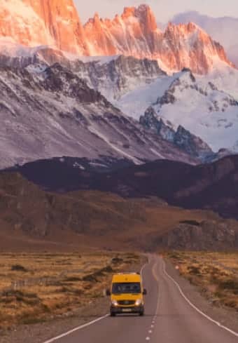 Gele camper op een open weg onder het besneeuwde Fitz Roy-massief in Patagonië
